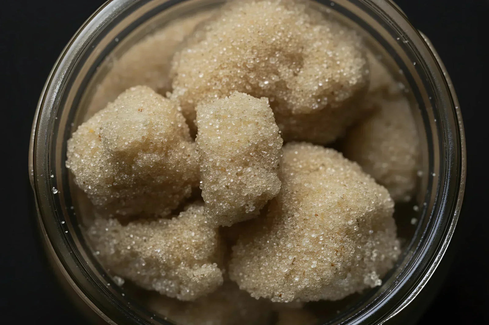 Glass jar filled with dry sifted cannabis trichome heads showing granular white crystalline texture illustrating isolated trichome starting material for solventless rosin pressing.